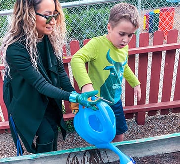 Teacher showing special needs child how to water a garden